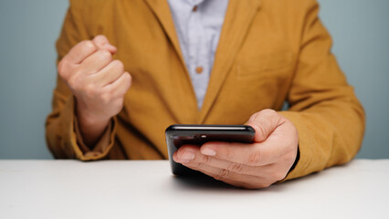 Cheerful man congratulating success clenched his fists. smartphone in hand