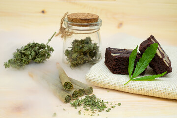 Pre-Roll cannabis joints and cake brownies with cannabis buds in a clear glass jar laying on the...