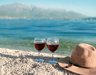 Two glasses of red wine and a straw hat on the beach in Montenegro