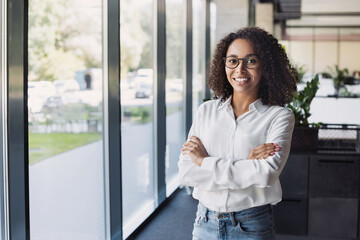 Young businesswoman portrait. Self confident young woman with crossed arms smiling at office. People, business casual, self confidence, leadership concepts