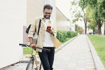 Fototapeta na wymiar Young handsome man walking with bike and smartphone in a city, Smiling student men with bicycle smiling and looking at mobile phone, Modern lifestyle, connection, travel, casual business concept