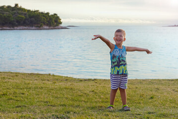Happy boy smiling ,spreading his arms to the sides at evening sunset on a  beach in Croatia.Happy lifestyle childhood concept - 582505421