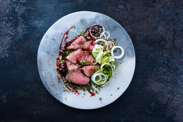 Traditional Commonwealth Sunday roast as sliced cold cuts roast beef with zucchini and capers in sweet amarena cherry sauce served as top view on a design plate