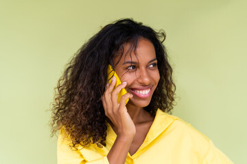 Beautiful african american woman in casual shirt on green background talk on mobile phone smile and laugh