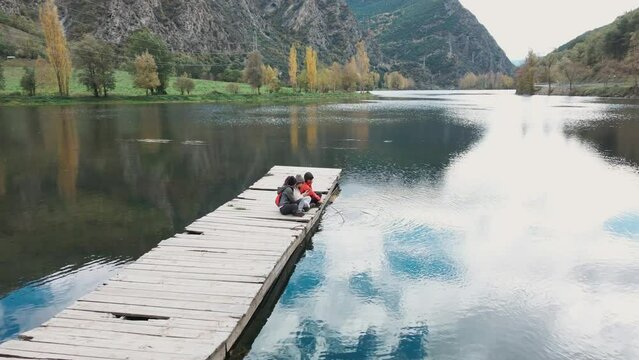 Video of pretty family looking at the horizon sitting on a pier on the lake