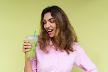 Young woman in casual wear isolated on green background positive vibes enjoying fresh ice green matcha tea with milk at hot summer day