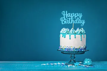 Fotobehang White happy birthday cake with teal ganache over a blue background © jfunk