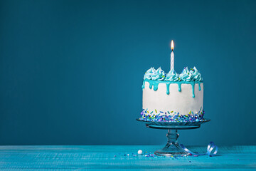 White cake with one lit birthday candle on a blue background - 582513885