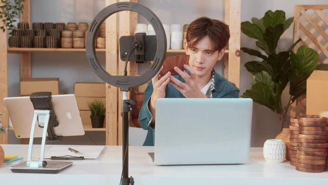 A young Asian man entrepreneur live streaming to sale craft products  to customers in his shop , Technology online business concept.