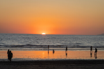 Fototapeta premium setting sun disappears below the horizon on the beach while people enjoy the light in Jaco, Costa Rica 