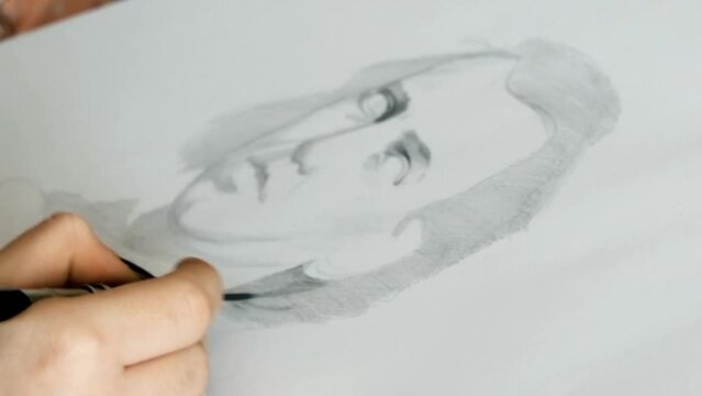 Close-up view of a young hand drawing a portrait of a man in pencil on a white paper. Portrait of Pianist musician Johannes Brahms