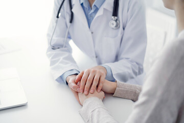 Doctor and patient sitting at the table in clinic office. The focus is on female physician's hands reassuring woman, only hands close up. Medicine concept