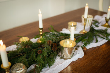 Elegant Holiday Themed Table Centerpiece Decor with White Linen Table Runner and Pine tree branches, and brass candles