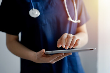 Doctor woman using tablet computer while standing near panorama window in clinic, close up. Physician or surgeon at work. Medicine concept