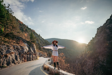 Obraz premium Woman road mountain. A woman in a white sweater, black boots and a hat walks along a winding alpine path between the mountains at sunset in late summer. The concept of travel.