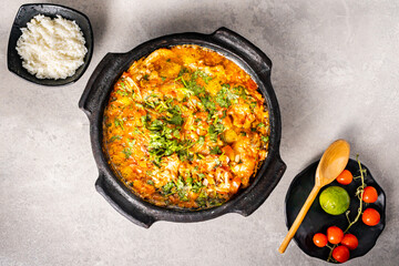 Delicious Brazilian fish moqueca with tomato, onion, olive oil, coriander and orocum seed. Made in clay pot on white table and black background.