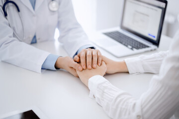 Doctor and patient sitting opposite each other at the table in clinic office. The focus is on female physician's hands reassuring woman, only hands, close up. Medicine concept