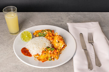 Delicious Brazilian fish moqueca with tomato, onion, olive oil, coriander and orocum seed. Served on a white porcelain plate with rice.