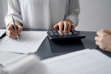 Woman accountant using a calculator and laptop computer while counting taxes for a client. Business...