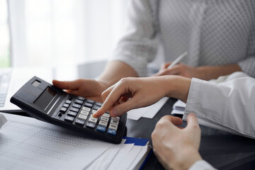 Woman accountant using a calculator and laptop computer while counting taxes for a client. Business...