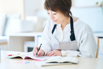 テキストで勉強するエプロン姿の女性 © maru54