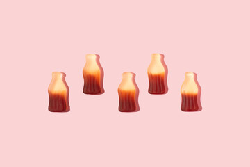 Bottle shaped gummy candies with sunlight shadows assorted in a line on pink background.