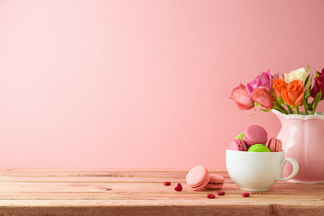 Macaroons french cookies on wooden table with rose flower bouquet over pink background.