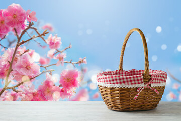 Empty picnic basket on wooden table over cherry blossom flowers background. Spring and easter mock up for design.