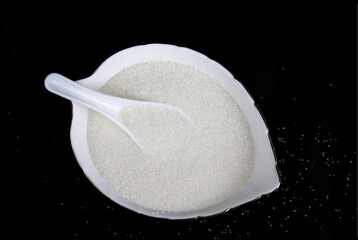 Bowl of white sugar on black background, top view