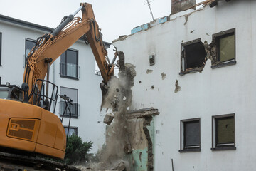 Demolition of a building. An excavator breaks an old house. A new house in the background