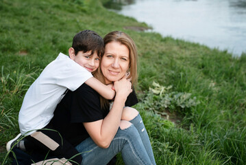 Mother and little son spend time together on the river bank in spring, the boy is not yet a...