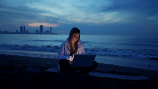 female freelancer is using a laptop on the beach of the sea in the evening slow mo
