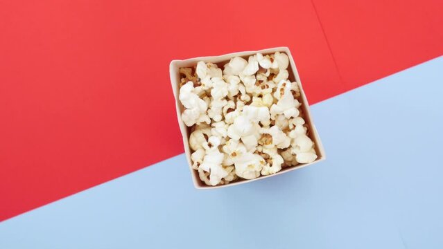 Popcorn in paper box on blue red surface revolving, junk food, entertainment, going out, time for watching films, movies. Close up, top view, rotation, 4K Ultra HD.