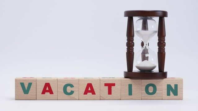 Hourglass with flowing sand inside stands on top of wooden cubes with letters that form for vacation, time to rest, measuring time, take break and relax. Close up, 4K Ultra HD.