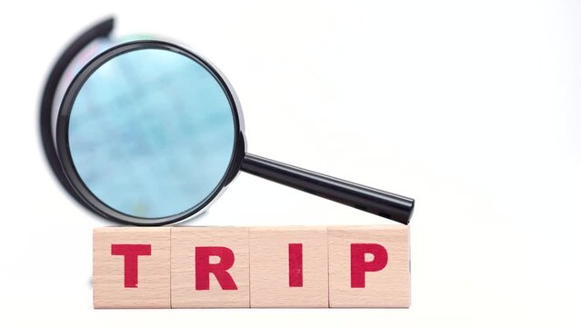 Wooden cubes create word trip, rotating globeth, magnifying glass on the white background