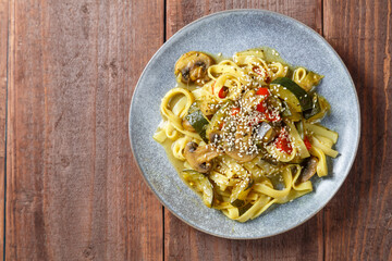 Gray plate with udon vegetables and gibi sprinkled with sesame seeds on a wooden table. save a place