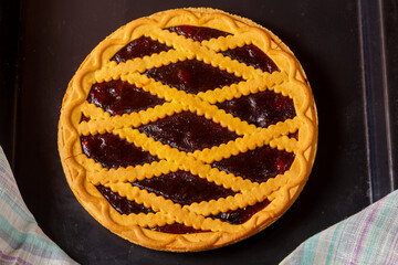 Shortcrust pastry cherry pie decorated with cherries and pastry grill on a baking sheet next to a towel.
