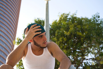 Portrait of a young man dressed in jeans and white t-shirt. The young man is sitting on a park...