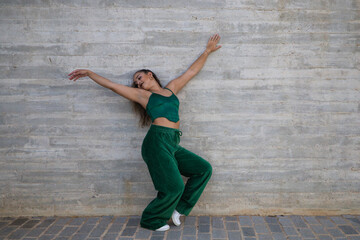 Latin woman, young and beautiful dancing modern dance on a background of gray cement in the street makes different expressions and postures. Concept dance, hip hop, dance, art, action, youth art.