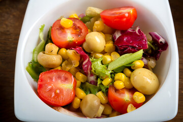 Vegetable salad with champignon corn and cherry tomato with avocado in a white plate.