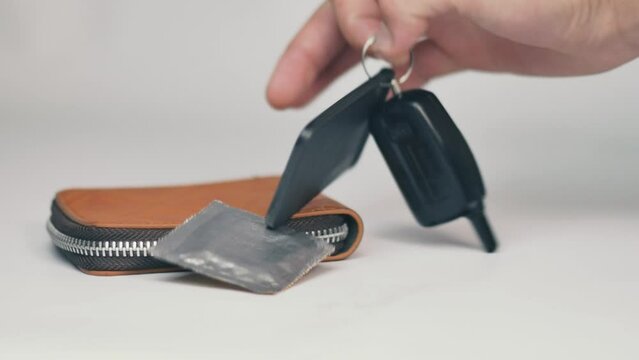 Male hand takes the car keys, a condom and a wallet on a white background. Planning for safe sex.