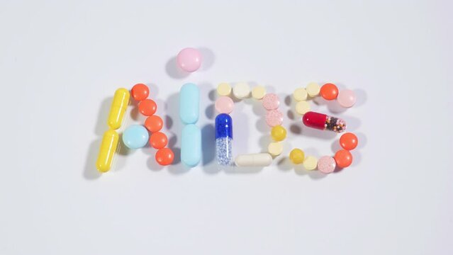 Stop motion animation of multicolored pills, capsules and tablets making word AIDS on white background. Consept of AIDS HIV treatment, protection, prevention.