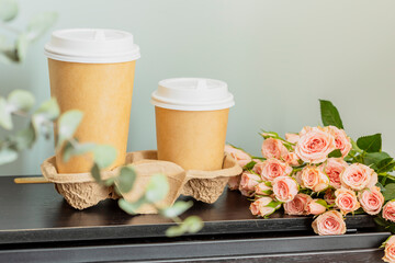 Spring romantic holiday composition with two disposable cups of coffee and bouquet of roses on wooden table. Dating or love concept. coffee to go. Mothers day, woman's day, birthday or valentines day