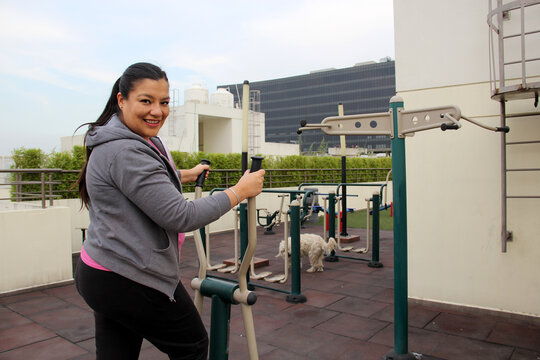 Adult 40-year-old Latina woman exercises on the roof garden of her apartment with shared public exercise equipment