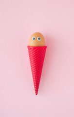 Colored ice cream cone and fresh chicken egg on pastel pink background. Minimal creative sweet food concept. Copy space.