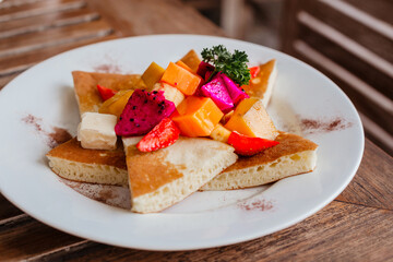 Delicious pancakes with cinnamon and fresh fruit on a white plate against the backdrop of a wooden table