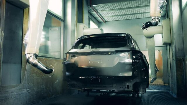 Robotic arms spray painting a vehicle body black at a car manufacturing factory