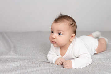 The baby lies on his stomach on the bed. A beautiful baby smiles. Mockup for advertising, design, celebration, postcards.