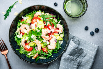 Strawberry, shrimp and herbs healthy salad with arugula, avocado and almond slices, gray kitchen table. Fresh useful dish for healthy eating