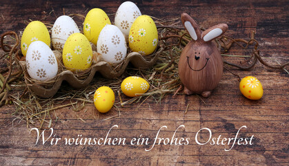 Grußkarte Frohe Ostern: Gelbe und weiße Ostereier in einer Eierschachtel mit dem Ostergruß wir...